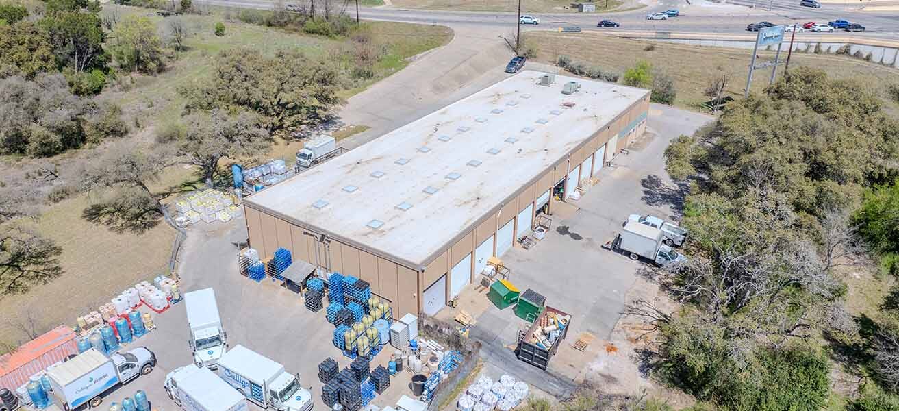 Exterior view of Brennan Investment Group’s newly acquired industrial outdoor storage properties in Texas, featuring functional warehouse buildings with grade-level doors, drive-thru access, and expansive outdoor storage areas in Austin and Houston.