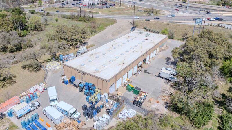 Exterior view of Brennan Investment Group’s newly acquired industrial outdoor storage properties in Texas, featuring functional warehouse buildings with grade-level doors, drive-thru access, and expansive outdoor storage areas in Austin and Houston.